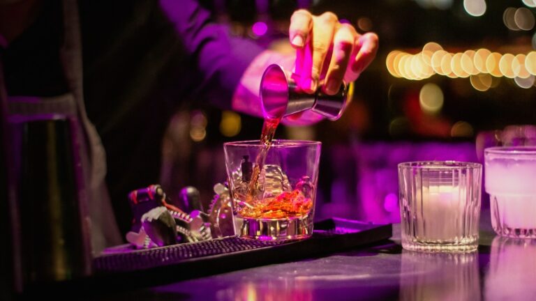 Bartender sirviendo un cóctel en una barra con neón morado